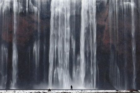 Silhouette of a man standing in front of a waterfall.の素材