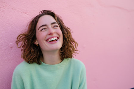 Portrait of a beautiful young woman smiling against a pink wall.の素材