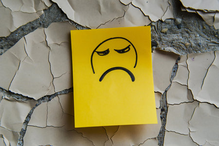 Yellow Sticky Note with Sad Face on Cracked Wood Background.の素材