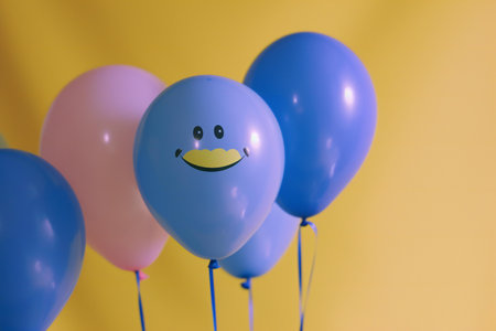 Blue and pink balloons with a smiley face on a yellow backgroundの素材