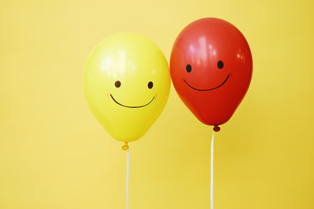 Two smiling balloons on yellow background. Concept of happiness and joy.の素材