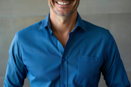 Close-up of smiling man in blue shirt against grey wall backgroundの素材