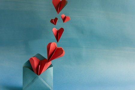 Paper hearts fly out of an envelope on a blue background. Valentine's Dayの素材