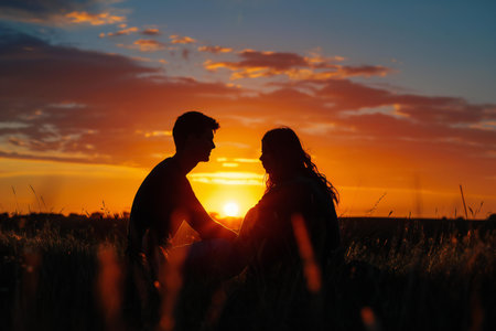 Silhouette of a loving couple sitting in the field at sunsetの素材