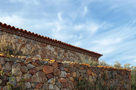Old stone wall with red tiled roof against blue cloudy sky.の素材