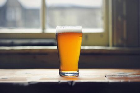 Glass of beer on a wooden table with a window in the backgroundの素材