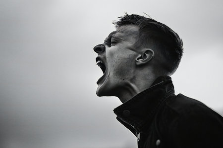 Portrait of a screaming young man in a black jacket on the background of the skyの素材