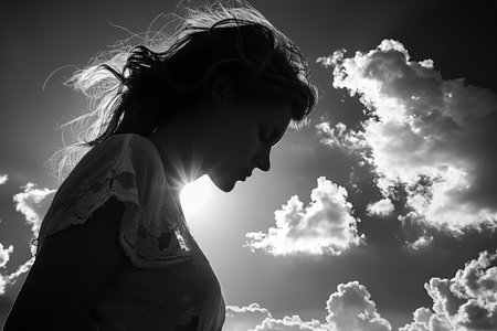 Silhouette of a beautiful young woman against the sky with cloudsの写真素材