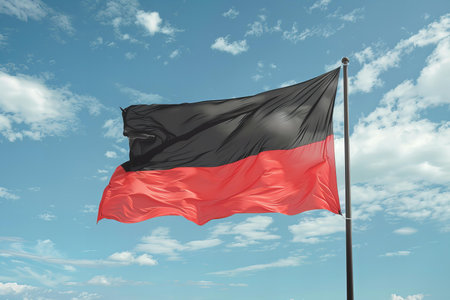 German flag waving in the wind against a blue sky with white cloudsの写真素材