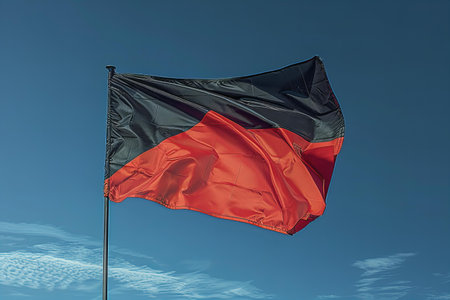 A red and black flag waving in the wind against a blue skyの写真素材