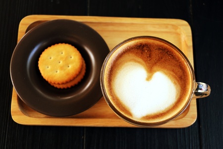 Cappuccino  in clear glass with heart shape foam on the top with biscuitの写真素材