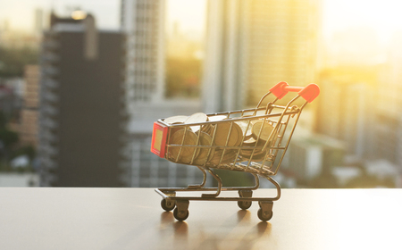 Shopping cart with coins on the table with blur building sunset background.Business concept.の写真素材