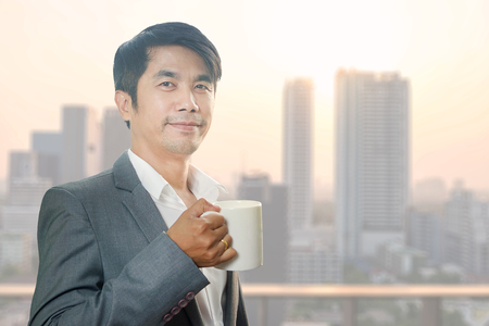 Asian Business Man relaxing and drinking hot coffee with blur building background at sunset time.の写真素材