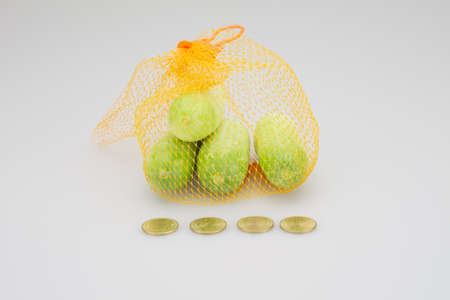 Cucumbers in orange mesh resting have gold coins as foreground on a white table.の写真素材