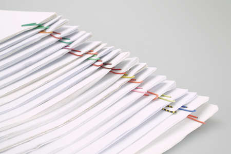 Colorful paper clip with pile of overload white paperwork and reports arranged on white table.