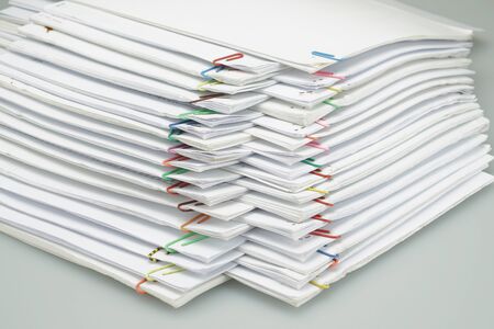 Colorful paper clip with pile of overload white paperwork and reports arranged on white table.