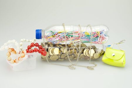 Colortul paperclip and gold coins are in plastic bottle with necklace, bracelet and wallet on white...