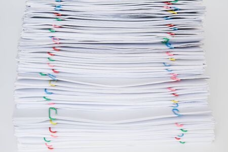 Colorful paper clip with pile of overload paper and reports place on white table.