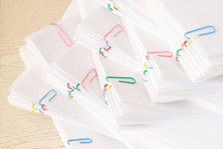Colorful paper clip with stack of overload paperwork and reports place on wooden table.