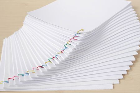 Colorful paperclip with pile of overload white paperwork and reports arranged on wood table.