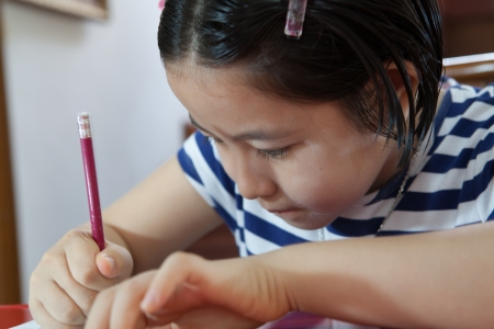 Young attractive female Asian student sitting at her desk and writingの写真素材