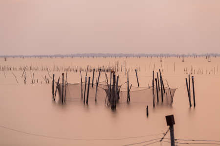 Wooden pier or jetty remains on a blue lake sunset and cloudy sky reflection on water.の写真素材