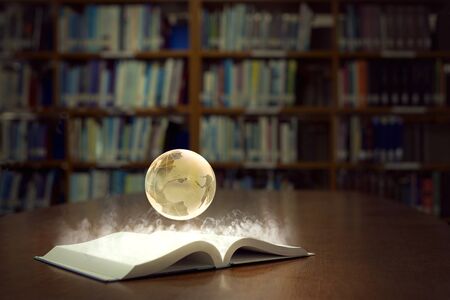 An open book glows brightly and reveals a globe of the world, in old self of book library university...