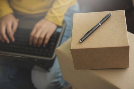 Woman using a computer while sitting at the modern working desk  by stack of cardboard boxes with living room.E-commerce, internet technology, or startup small business concept.の写真素材