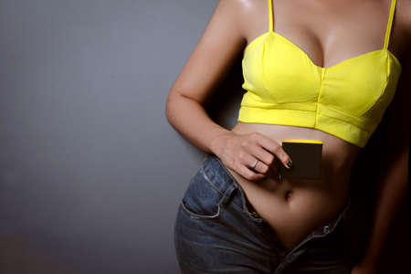 Young woman holding a blackbox in yellow singlet and jeans texas shorts on dark background.の写真素材