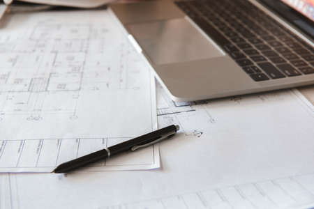 Close-up of blueprints with sketches of projects, laptop and a pen.の写真素材