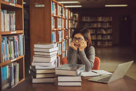 Bored young female student sitting at table in a campus open space library. Education conceptの写真素材