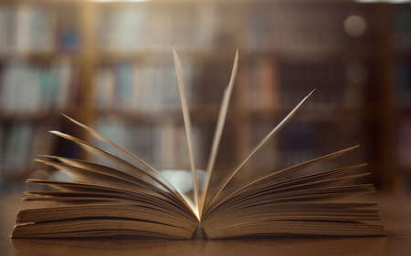 Old open book on the table a bookshelf background for academic education learning concept.の写真素材