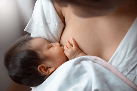Close-up young woman breastfeeding her baby on blurred background.の写真素材