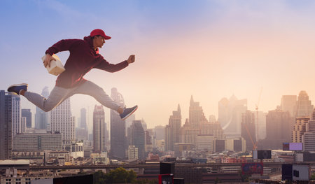 Delivery man holding cardboard boxes and jumping high on city background. Online Shopping and Express delivery Concept.の写真素材
