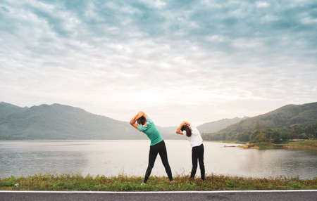 Mom and girl child doing stretching before workout outdoor at mountain lake in the morning to get a healthy lifestyle.の写真素材