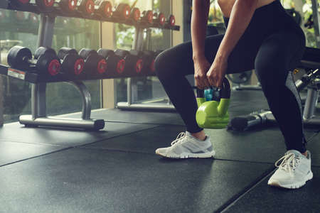 Woman exercising with kettlebell while being in squats position at the gym.の写真素材