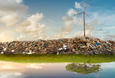 Wind turbines on top of garbage mountains reflection with the green tree on green mountains in quiet water.の写真素材