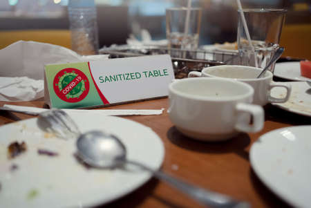 Empty dishes on the dining table with sanitized table sign in a restaurant, COVID-19 pandemic,...