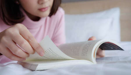 Young woman lying and reading book on bed.の写真素材