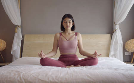 Woman in sportsware practice yoga lotus pose to meditation at home, Wellness woman doing yoga for breathing and meditation comfortable and relax.の写真素材