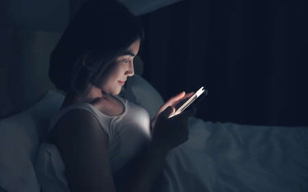 Woman sending messages on cellphone and lying on bed.の写真素材