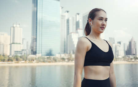 Sport woman wearing wireless headphones and stretching muscles before running in city, warmup exercise.の写真素材