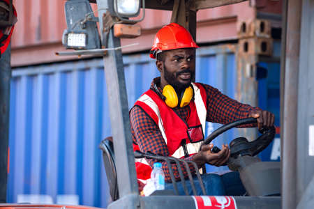 Male worker in uniform and helmet driving and operating on diesel container forklift truck at...