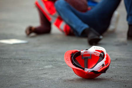 Red hard safety helmet hat for engineer on concrete ground with African-American male engineers injured the accident from working  blurred image background.の写真素材