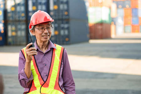 A senior elderly Asian worker engineer wearing safety vest and helmet standing and holding radio...