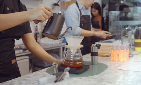 A female cafe operator wearing an apron pours hot water over roasted coffee grounds to prepare coffee for customers in the shop.の写真素材