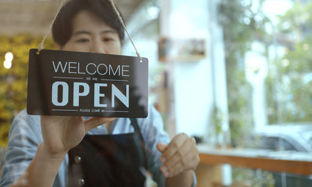 Business owner asian woman turning Welcome We're Open sign on fronton glass door store.