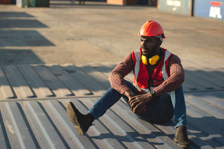 African American male technician or engineer. Sit near a container and look tired and sleepy or unemployed. Logistics industrial cargo mover concept.の写真素材