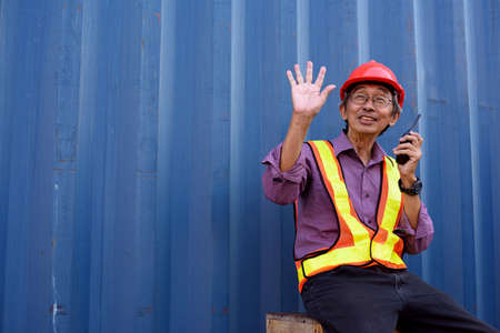 A senior elderly Asian worker engineer wearing safety vest and helmet standing and holding radio...