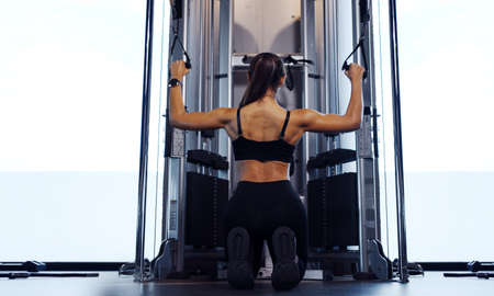 Sporty woman exercising on multistation at gym for arm and shoulders muscles. Fitness exercising in...